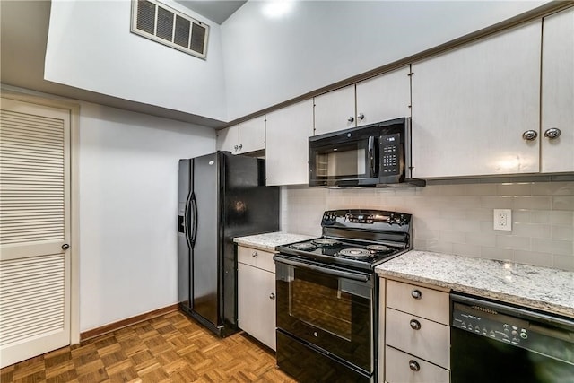 kitchen with decorative backsplash, black appliances, light stone countertops, light parquet floors, and white cabinetry