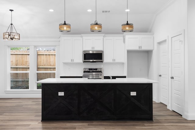 kitchen with a center island with sink, white cabinetry, stainless steel appliances, and hanging light fixtures