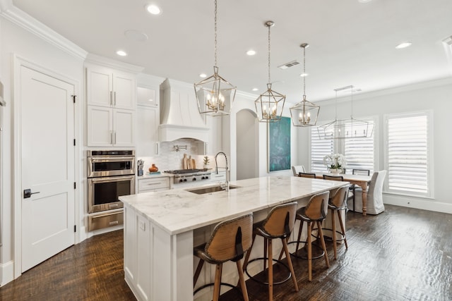 kitchen with stainless steel appliances, a large island with sink, white cabinets, and hanging light fixtures