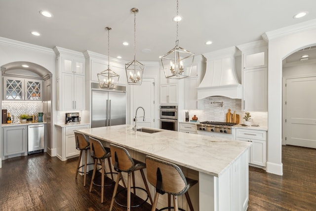 kitchen with white cabinetry, sink, stainless steel appliances, a large island with sink, and custom exhaust hood