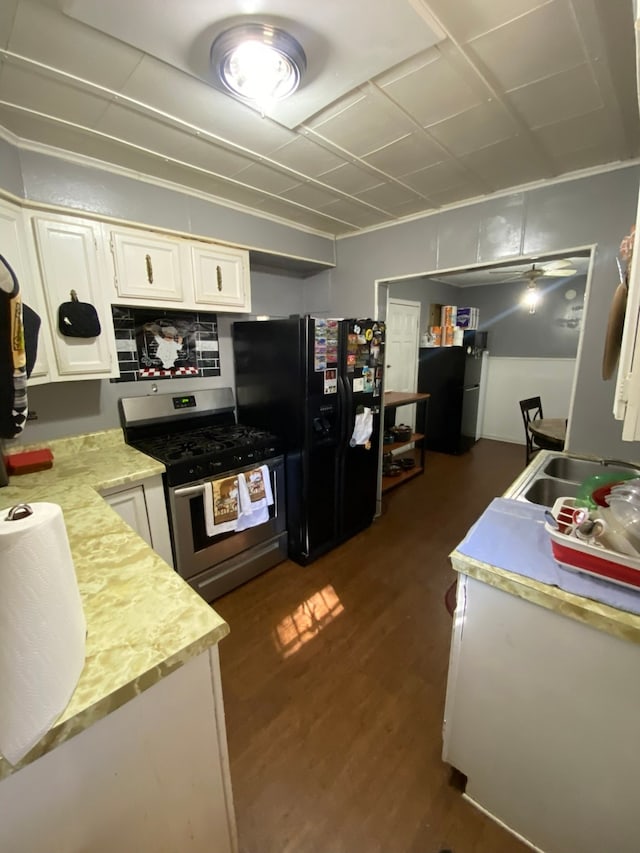 kitchen with black refrigerator with ice dispenser, stainless steel gas range oven, dark hardwood / wood-style flooring, sink, and white cabinets