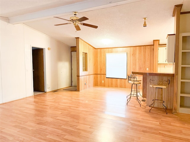 interior space featuring light hardwood / wood-style flooring, ornamental molding, lofted ceiling with beams, a textured ceiling, and wood walls