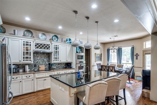 kitchen featuring white cabinetry, appliances with stainless steel finishes, a kitchen bar, decorative light fixtures, and a kitchen island with sink