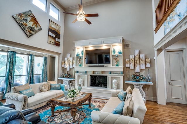 living room featuring ornamental molding, wood-type flooring, ceiling fan, and a towering ceiling