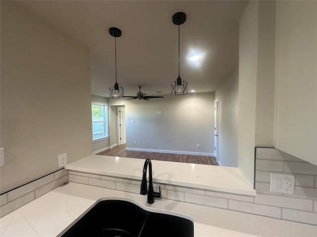 kitchen featuring light stone counters, pendant lighting, sink, hardwood / wood-style floors, and ceiling fan