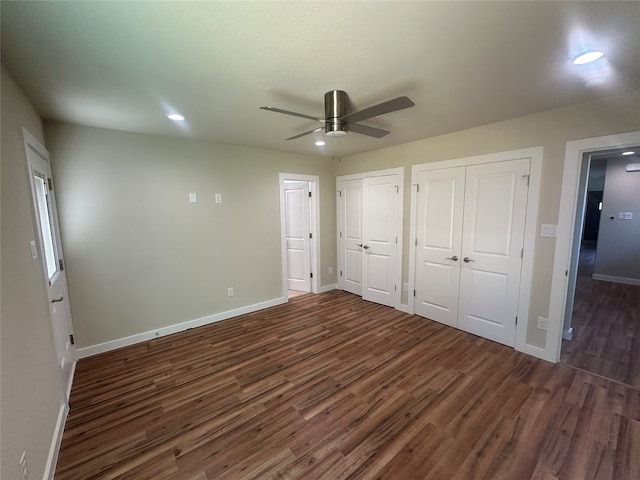 unfurnished bedroom with dark wood-type flooring, ceiling fan, and two closets