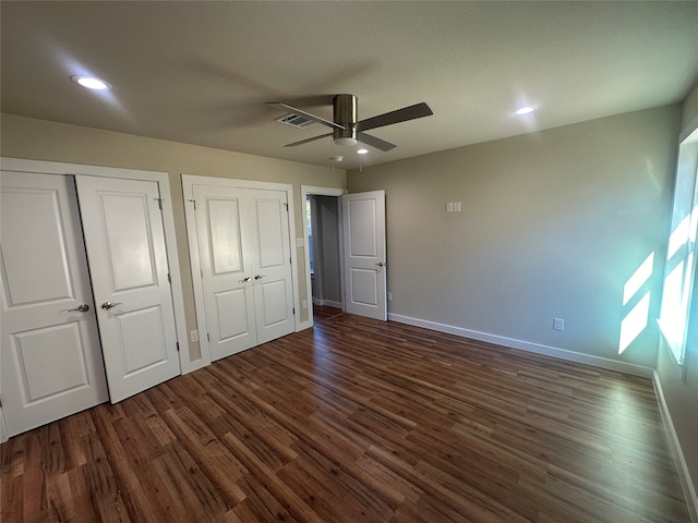 unfurnished bedroom with dark wood-type flooring, ceiling fan, and multiple closets