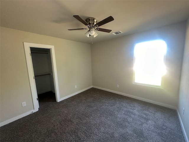 unfurnished bedroom featuring a closet, a spacious closet, dark carpet, and ceiling fan