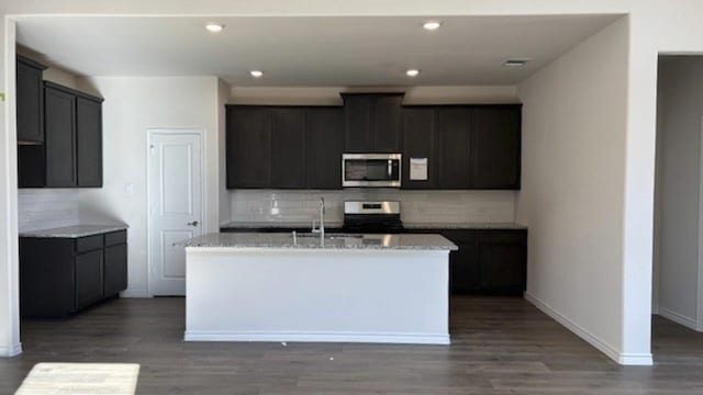 kitchen featuring stainless steel appliances, sink, backsplash, dark hardwood / wood-style floors, and a kitchen island with sink