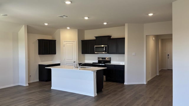 kitchen featuring a center island with sink, visible vents, dark cabinets, stainless steel appliances, and light countertops