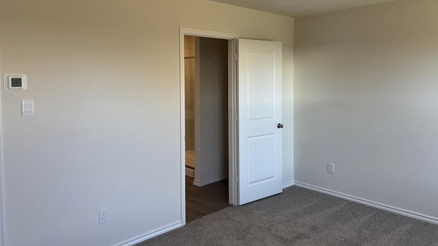 unfurnished bedroom with dark carpet and baseboards