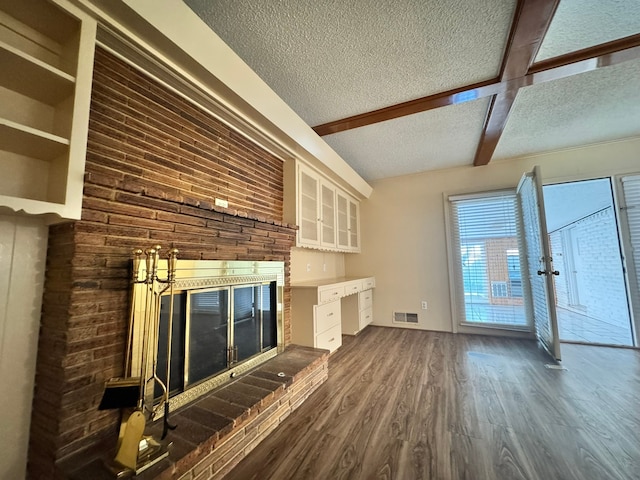 unfurnished living room featuring a textured ceiling, beam ceiling, dark hardwood / wood-style floors, and a brick fireplace