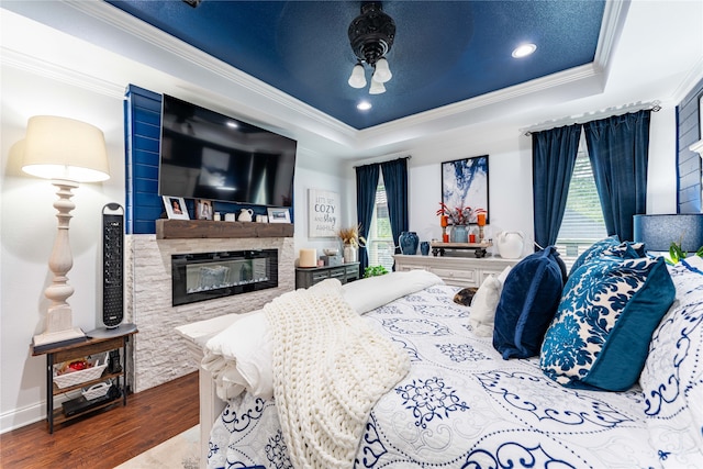 bedroom featuring wood-type flooring, a tray ceiling, a stone fireplace, and multiple windows