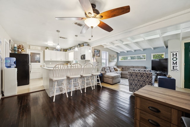 kitchen featuring vaulted ceiling with beams, black refrigerator, white cabinets, a kitchen breakfast bar, and dark hardwood / wood-style floors