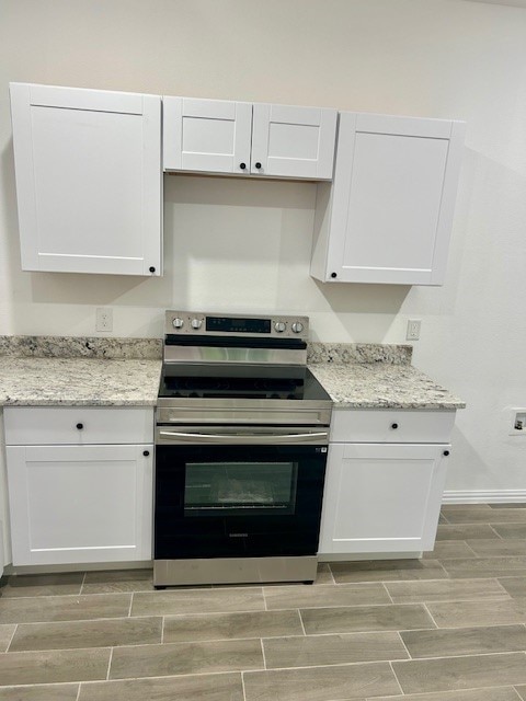 kitchen featuring light hardwood / wood-style flooring, white cabinets, light stone counters, and electric range