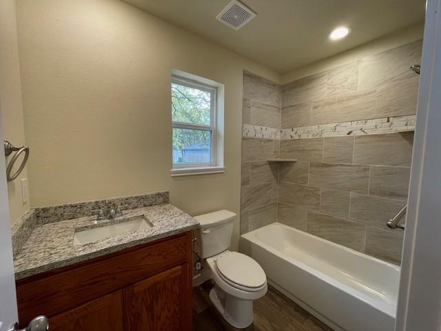 full bathroom featuring hardwood / wood-style flooring, vanity, toilet, and tiled shower / bath combo