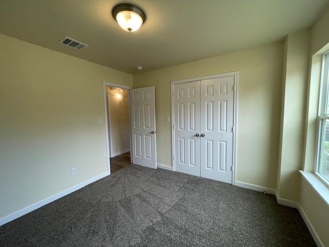 unfurnished bedroom with dark carpet and a closet