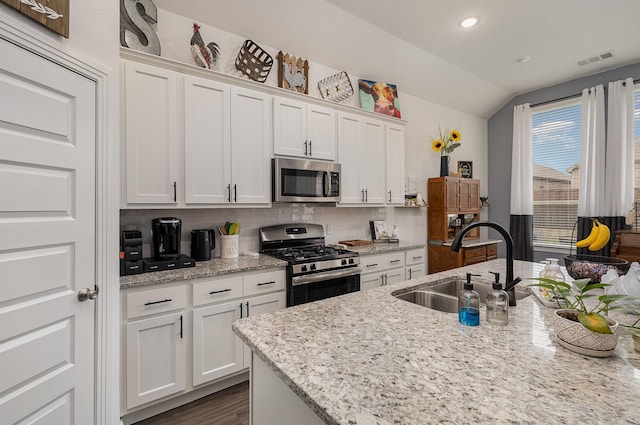 kitchen with white cabinets, sink, vaulted ceiling, light stone countertops, and stainless steel appliances