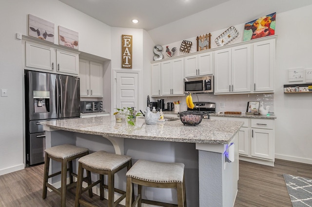 kitchen with light stone countertops, a kitchen island with sink, stainless steel appliances, a breakfast bar area, and decorative backsplash