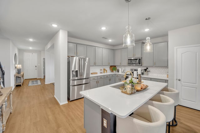 kitchen featuring stainless steel appliances, light hardwood / wood-style floors, a kitchen island with sink, and pendant lighting