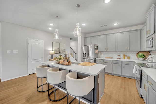 kitchen featuring light wood-type flooring, appliances with stainless steel finishes, hanging light fixtures, a kitchen breakfast bar, and a kitchen island with sink