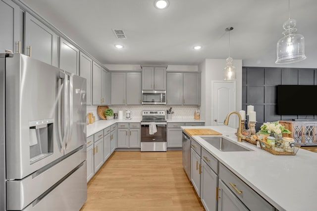 kitchen featuring light hardwood / wood-style floors, sink, appliances with stainless steel finishes, decorative light fixtures, and gray cabinetry