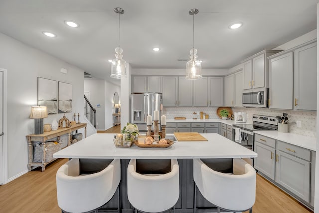 kitchen with light hardwood / wood-style floors, a kitchen island with sink, decorative light fixtures, and appliances with stainless steel finishes