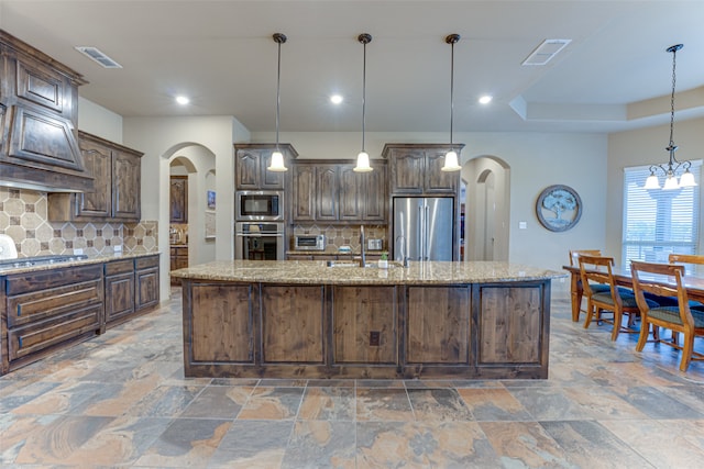 kitchen with stainless steel appliances, backsplash, dark brown cabinetry, pendant lighting, and a kitchen island with sink