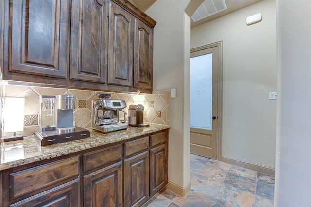 kitchen with dark brown cabinets, backsplash, and light stone countertops