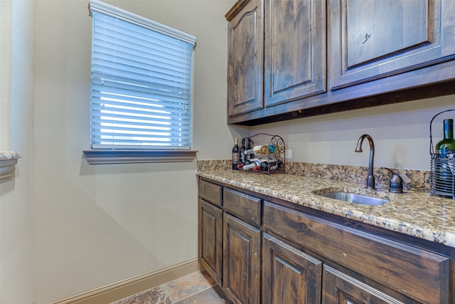 kitchen with dark brown cabinetry, sink, and light stone counters