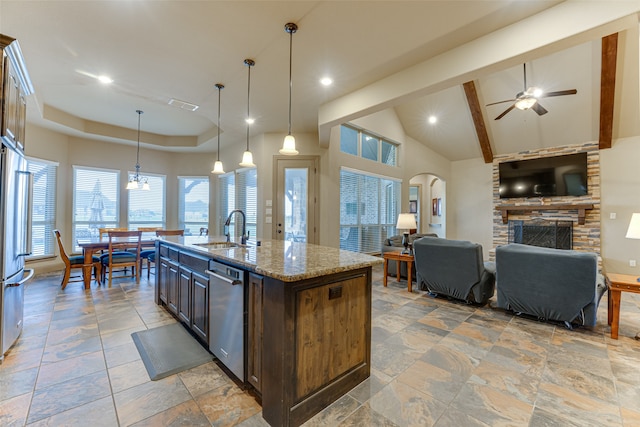 kitchen featuring light stone counters, hanging light fixtures, sink, an island with sink, and stainless steel dishwasher