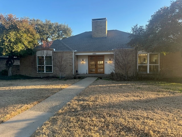 view of front of house with brick siding, french doors, roof with shingles, a chimney, and a front yard