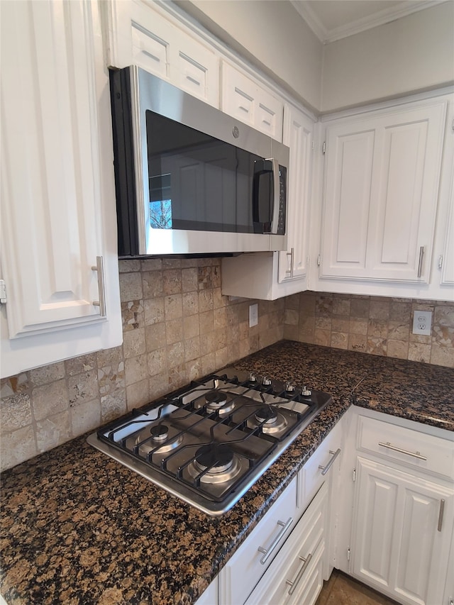 kitchen featuring white cabinetry, dark stone counters, decorative backsplash, gas stovetop, and crown molding