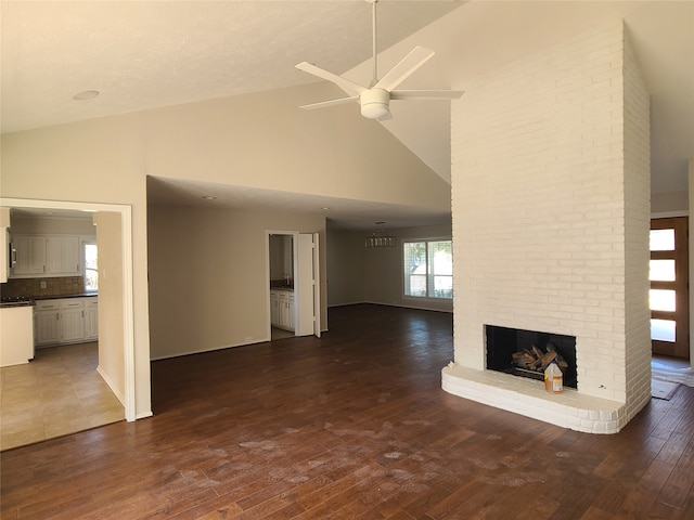 unfurnished living room featuring ceiling fan, dark hardwood / wood-style floors, high vaulted ceiling, and a brick fireplace