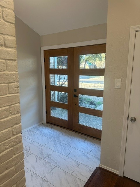 doorway with lofted ceiling, marble finish floor, french doors, and baseboards