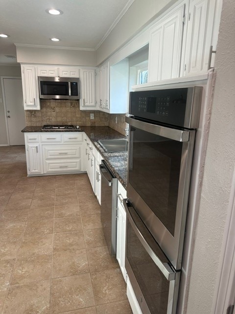 kitchen with white cabinets, ornamental molding, appliances with stainless steel finishes, decorative backsplash, and dark stone counters