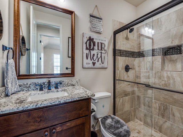 bathroom featuring a shower with door, vanity, and toilet