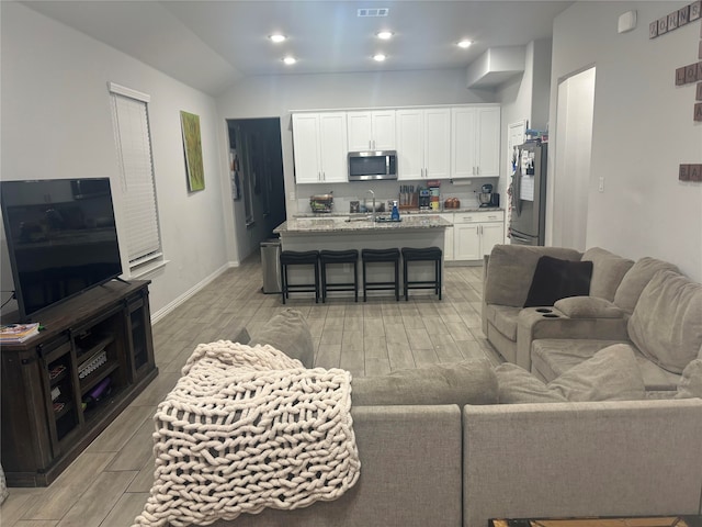 living room with sink, light hardwood / wood-style flooring, and lofted ceiling