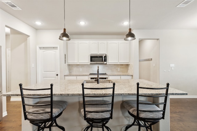 kitchen featuring tasteful backsplash, white cabinetry, an island with sink, and a kitchen breakfast bar