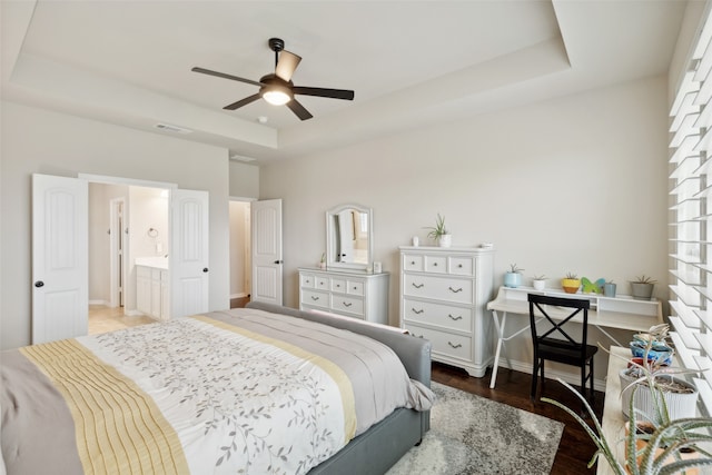 bedroom with connected bathroom, a tray ceiling, hardwood / wood-style flooring, and ceiling fan