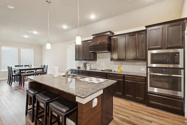 kitchen featuring a center island with sink, pendant lighting, sink, light hardwood / wood-style floors, and custom exhaust hood