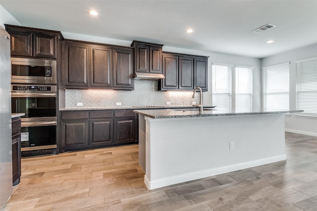 kitchen featuring dark brown cabinets, a center island with sink, and stainless steel microwave