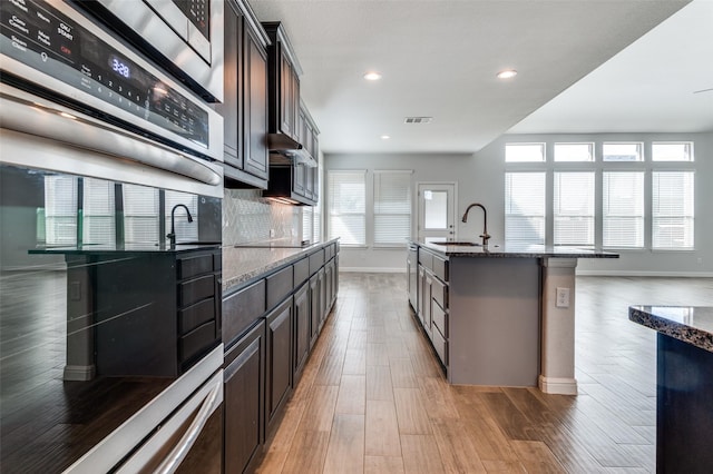 kitchen with dark brown cabinets, an island with sink, and plenty of natural light