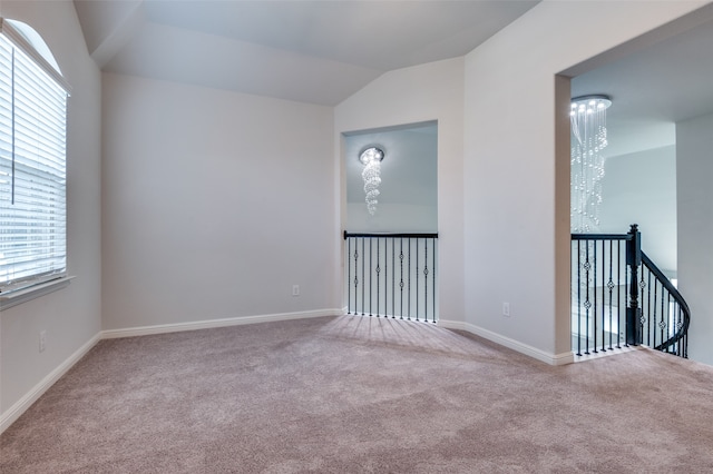 carpeted spare room featuring plenty of natural light, lofted ceiling, and an inviting chandelier