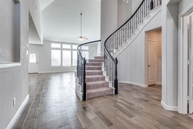 foyer entrance featuring ceiling fan, wood-type flooring, and a towering ceiling