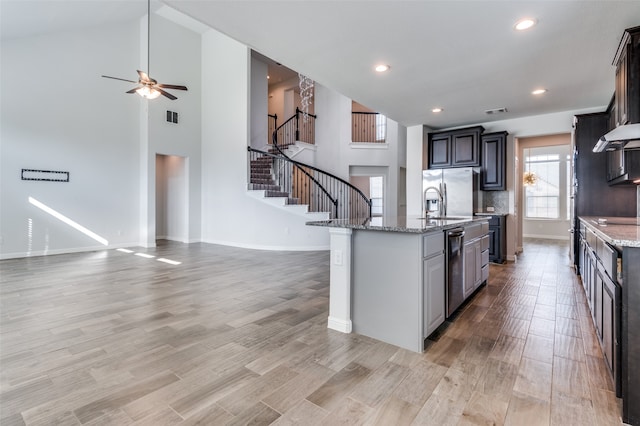 kitchen featuring stainless steel fridge, light wood-type flooring, light stone counters, and an island with sink