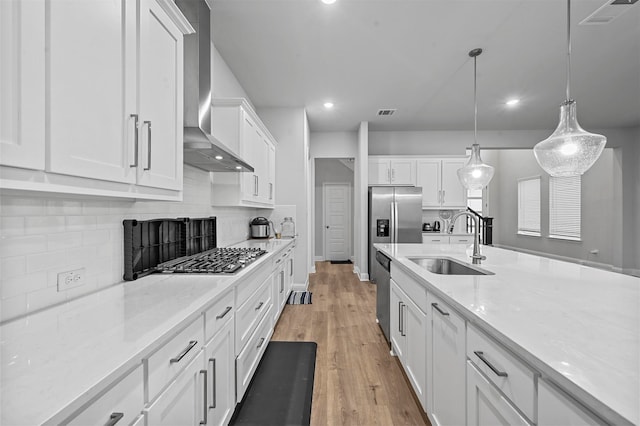 kitchen with appliances with stainless steel finishes, decorative light fixtures, sink, white cabinets, and wall chimney exhaust hood