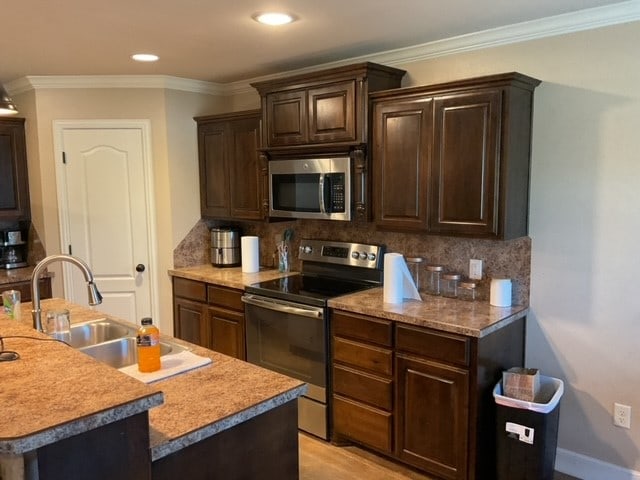 kitchen featuring an island with sink, crown molding, backsplash, and appliances with stainless steel finishes