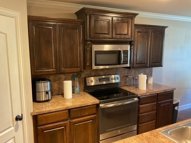 kitchen featuring tasteful backsplash, appliances with stainless steel finishes, dark brown cabinets, and ornamental molding