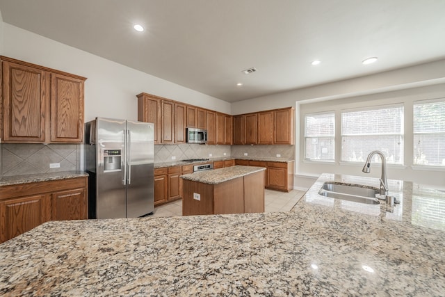 kitchen with appliances with stainless steel finishes, light tile patterned floors, light stone countertops, sink, and a center island